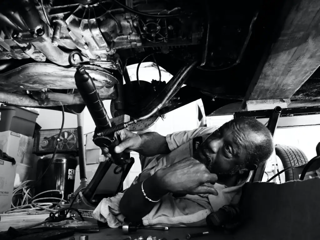 black and white image of a man underneath a car working 