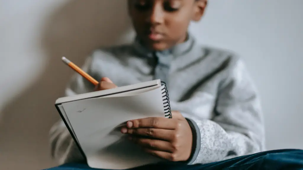 child writing in a notebook with a pencil