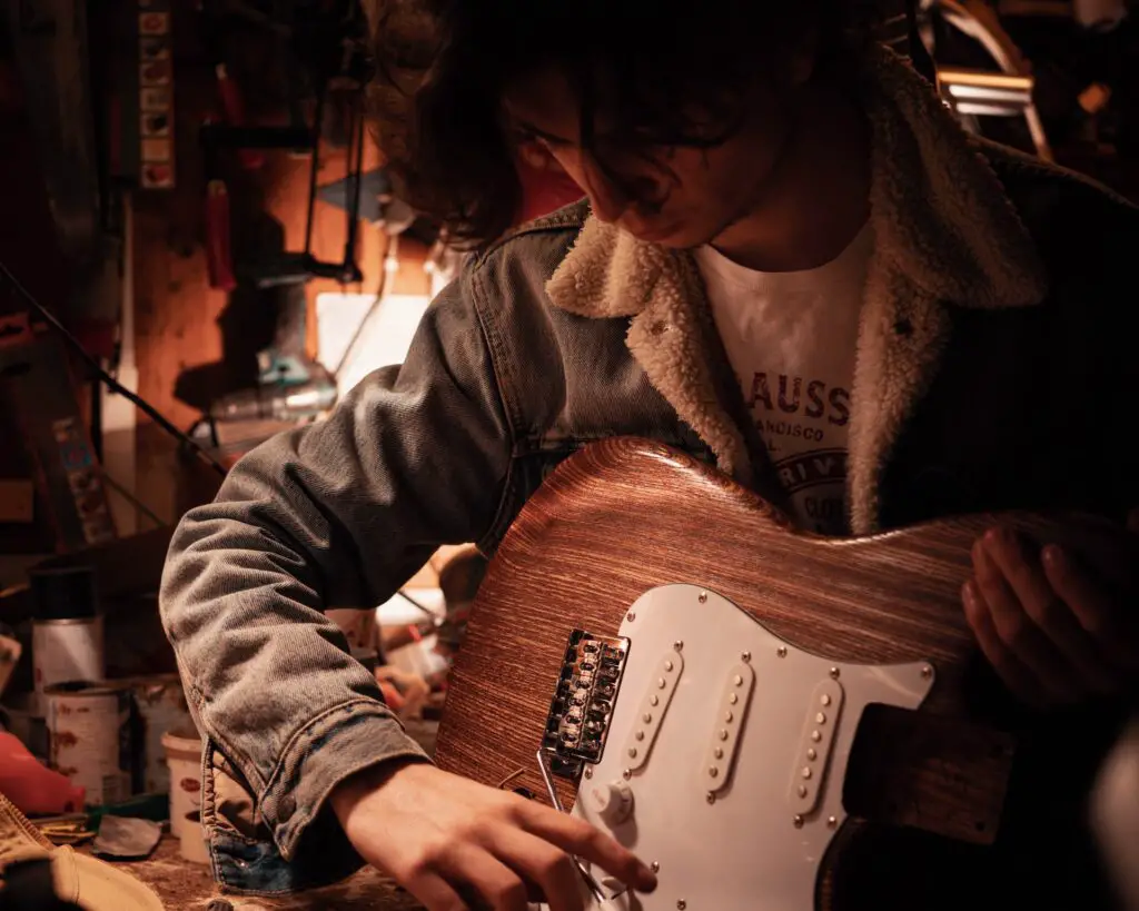 young man in jean jacket putting together an electric guitar