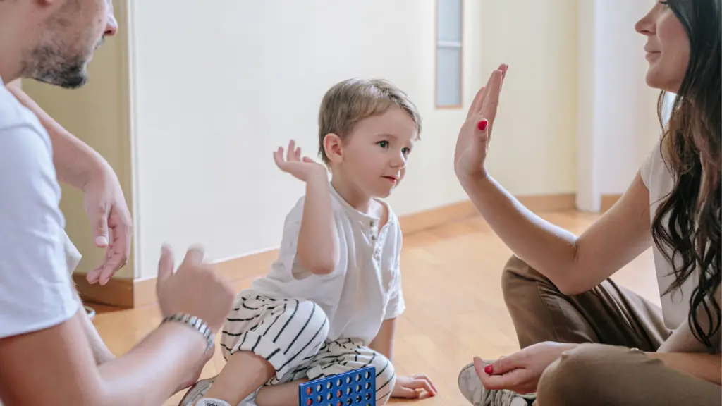 young boy high fiving mom while sitting with mom and day on the floor playing connect four
