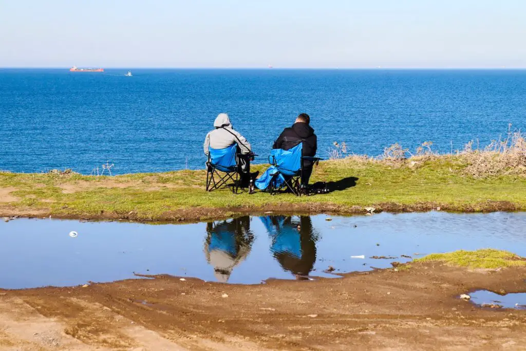 two men sitting in lawn chairs near the water