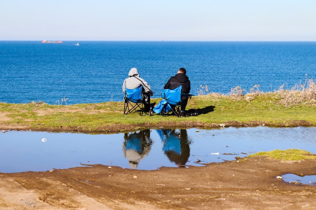 two men sitting in lawn chairs near the water