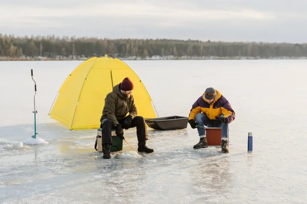 two men ice fishing, yellow tent in background