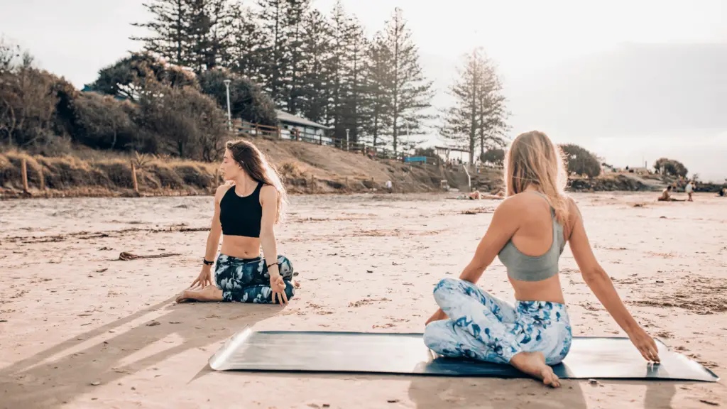 two women doing yoga on the beach; beach hobby