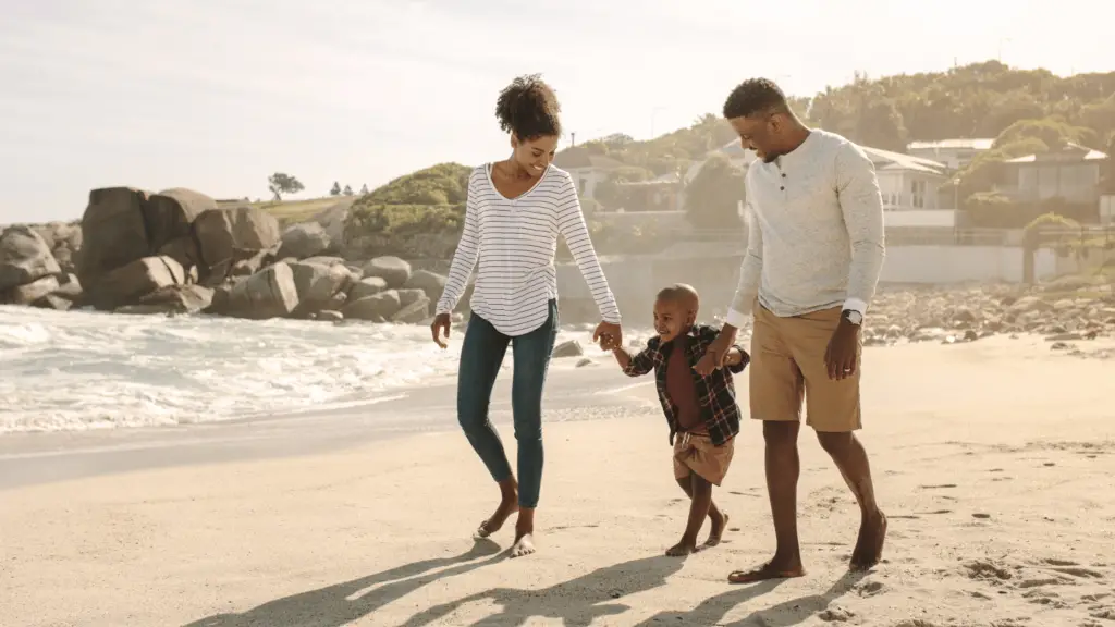 family of three walking with their young child at the beach