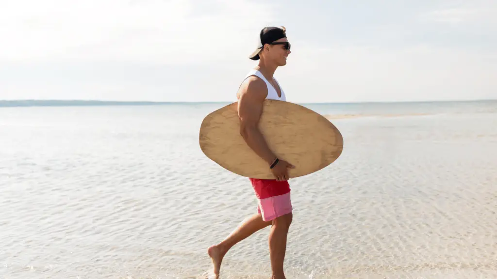 man walking with a skimboard at the waters edge 