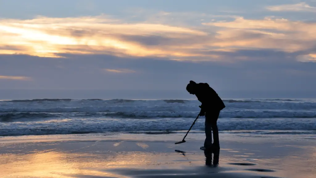 woman metal detecting at the beach at sunset