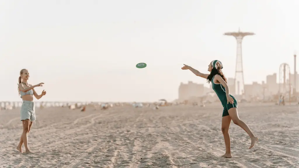 two women throwing a frisbee on the beach; beach hobby